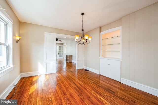 unfurnished dining area with an inviting chandelier, built in shelves, baseboards, and hardwood / wood-style floors