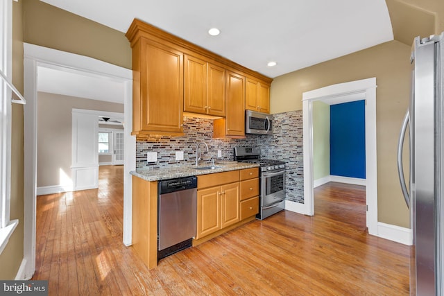 kitchen with light wood-style flooring, appliances with stainless steel finishes, decorative backsplash, and a sink