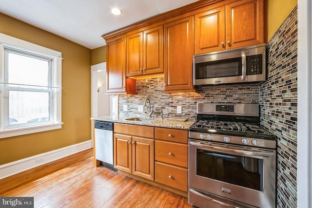 kitchen with stainless steel appliances, a sink, light wood-type flooring, backsplash, and light stone countertops