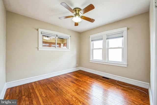 spare room featuring hardwood / wood-style flooring, baseboards, visible vents, and a ceiling fan