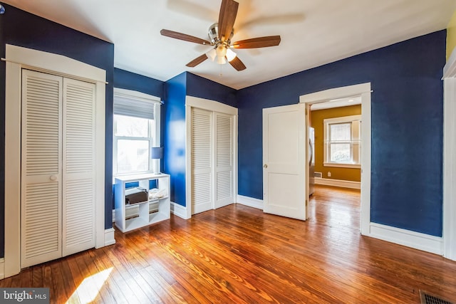 unfurnished bedroom featuring hardwood / wood-style floors, multiple windows, visible vents, and multiple closets