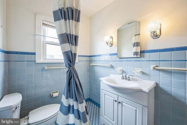 bathroom with tile walls, wainscoting, vanity, and toilet