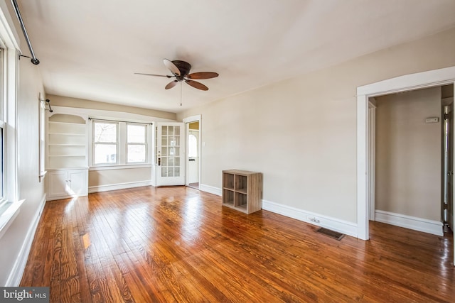 unfurnished living room featuring built in shelves, visible vents, a ceiling fan, baseboards, and hardwood / wood-style flooring