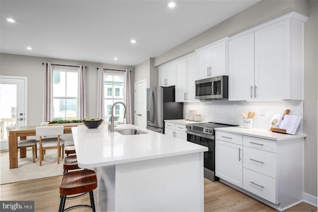 kitchen featuring light wood finished floors, stainless steel appliances, a sink, an island with sink, and a kitchen bar