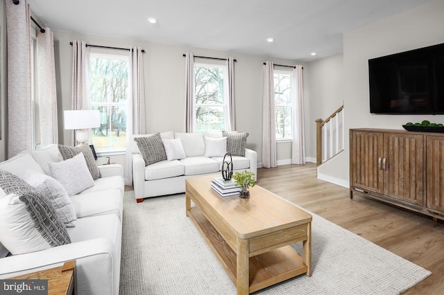 living room with a wealth of natural light, light wood-type flooring, recessed lighting, and stairs