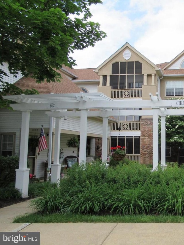 rear view of property featuring a pergola and a balcony