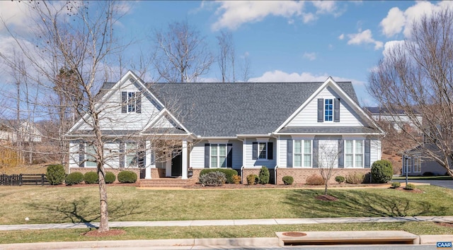 view of front of home featuring a shingled roof, a front yard, brick siding, and fence