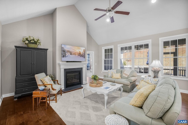 living area featuring dark wood-style floors, a ceiling fan, a glass covered fireplace, high vaulted ceiling, and baseboards