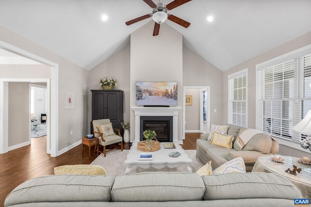 living room with a glass covered fireplace, ceiling fan, wood finished floors, high vaulted ceiling, and baseboards