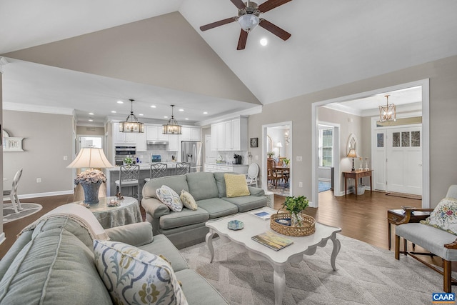 living room featuring high vaulted ceiling, ceiling fan with notable chandelier, wood finished floors, baseboards, and ornamental molding