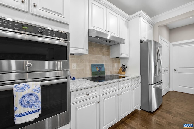 kitchen with under cabinet range hood, stainless steel appliances, white cabinets, decorative backsplash, and dark wood-style floors