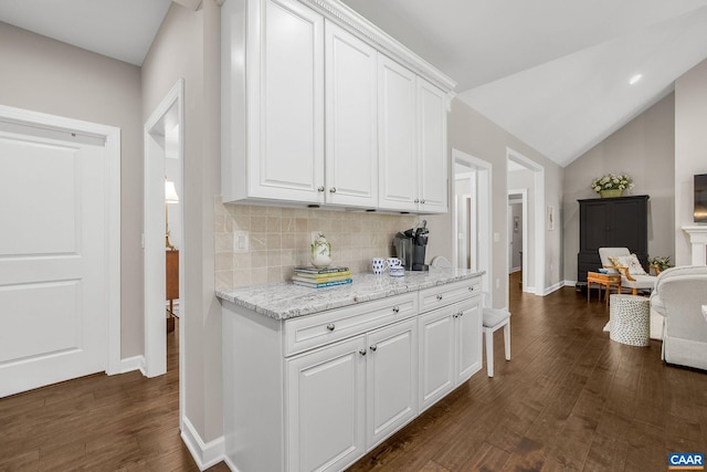 kitchen featuring baseboards, dark wood-type flooring, vaulted ceiling, white cabinetry, and backsplash