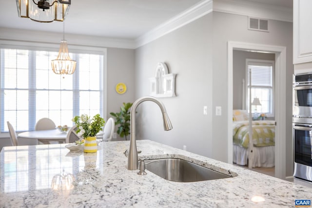 kitchen with light stone counters, a sink, visible vents, decorative light fixtures, and crown molding