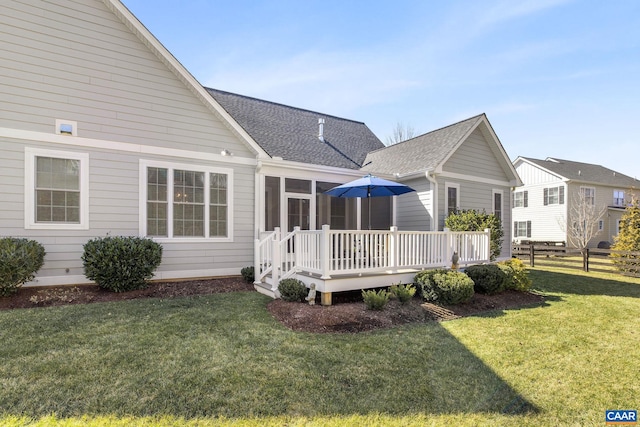 rear view of house with a lawn, a sunroom, roof with shingles, fence, and a deck