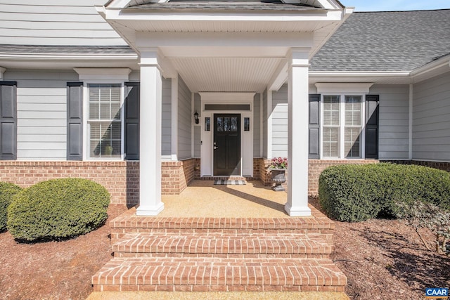 view of exterior entry with brick siding and a shingled roof