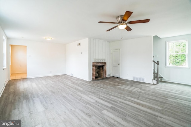 unfurnished living room with stairs, a brick fireplace, visible vents, and wood finished floors