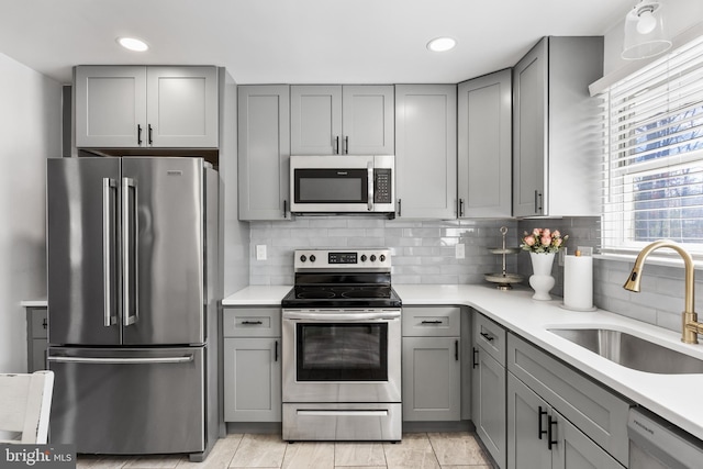 kitchen featuring decorative backsplash, appliances with stainless steel finishes, gray cabinets, and a sink