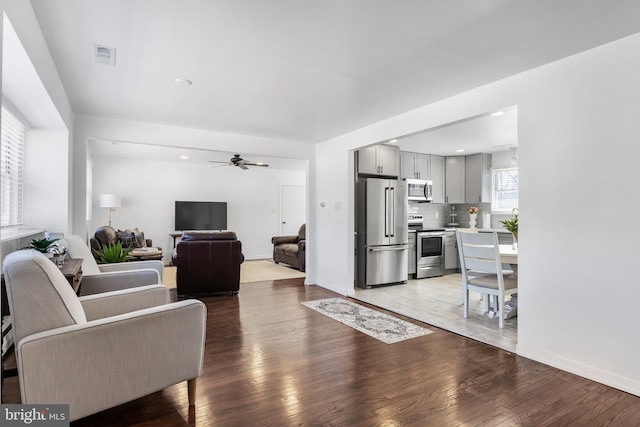 living room featuring baseboards, a ceiling fan, visible vents, and light wood-style floors