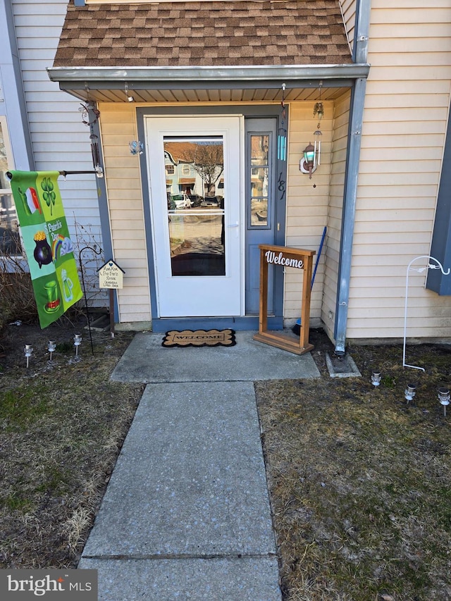 view of exterior entry featuring roof with shingles