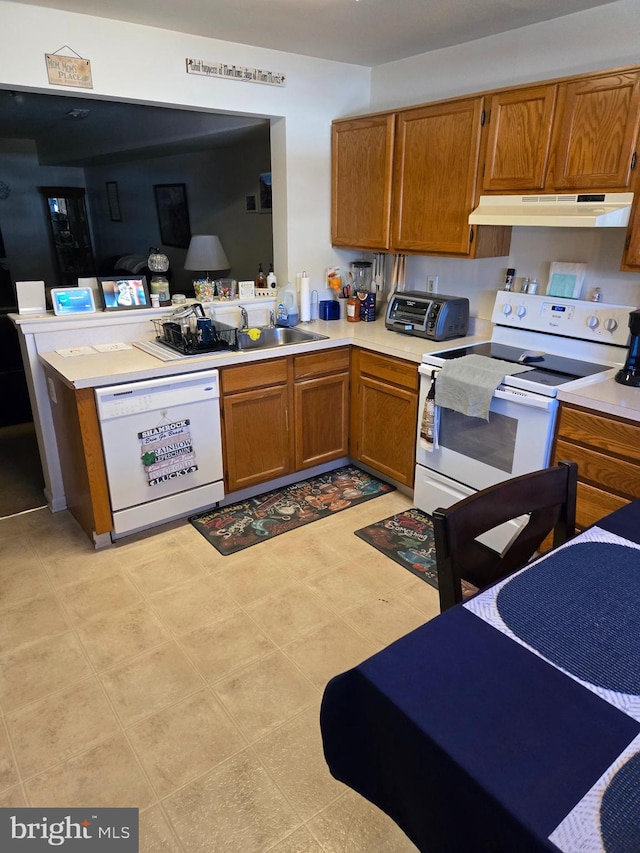 kitchen with light countertops, white appliances, brown cabinetry, and under cabinet range hood