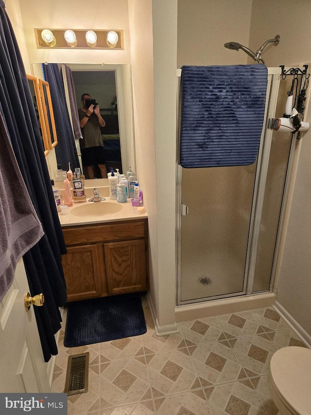 bathroom featuring toilet, vanity, visible vents, baseboards, and a stall shower