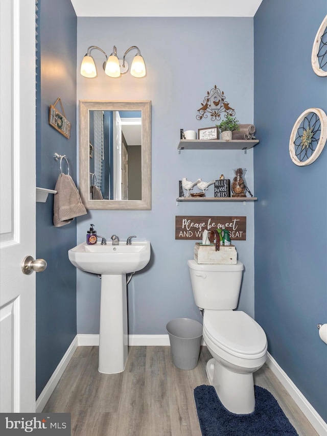 half bathroom with a sink, wood finished floors, toilet, and baseboards