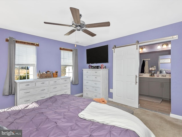 carpeted bedroom featuring baseboards, multiple windows, ensuite bathroom, and a barn door