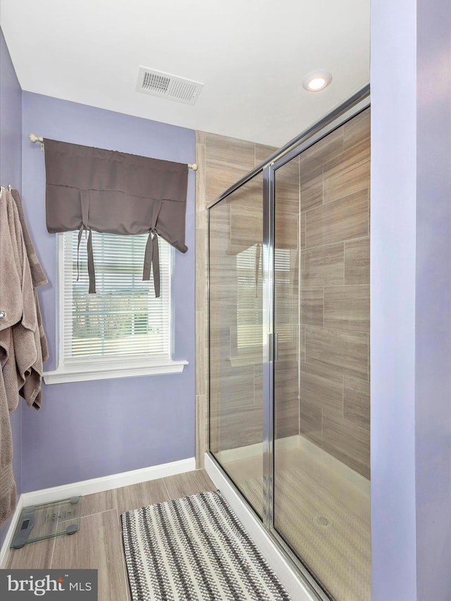 bathroom with a stall shower, wood finished floors, visible vents, and baseboards