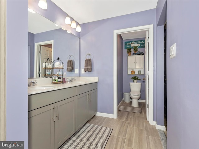 bathroom featuring double vanity, a sink, toilet, and baseboards