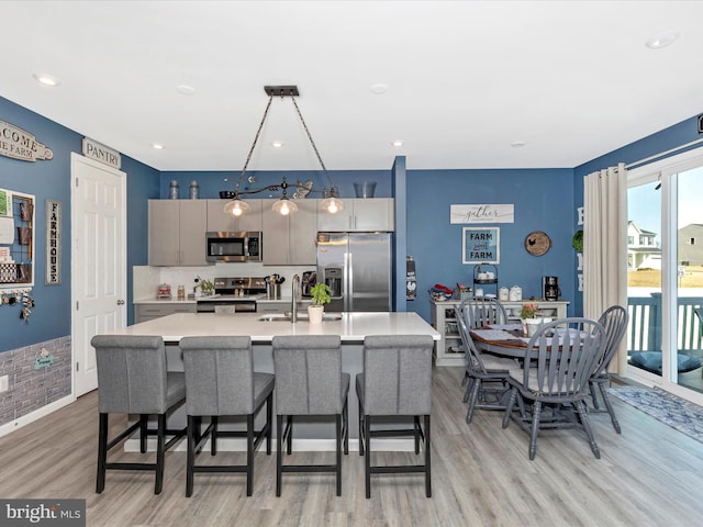 kitchen featuring a breakfast bar area, a kitchen island with sink, stainless steel appliances, a sink, and light countertops