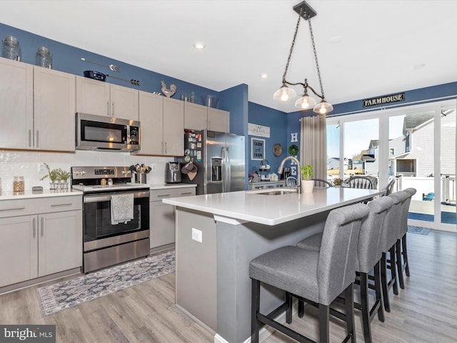 kitchen with decorative backsplash, appliances with stainless steel finishes, light countertops, light wood-type flooring, and a sink