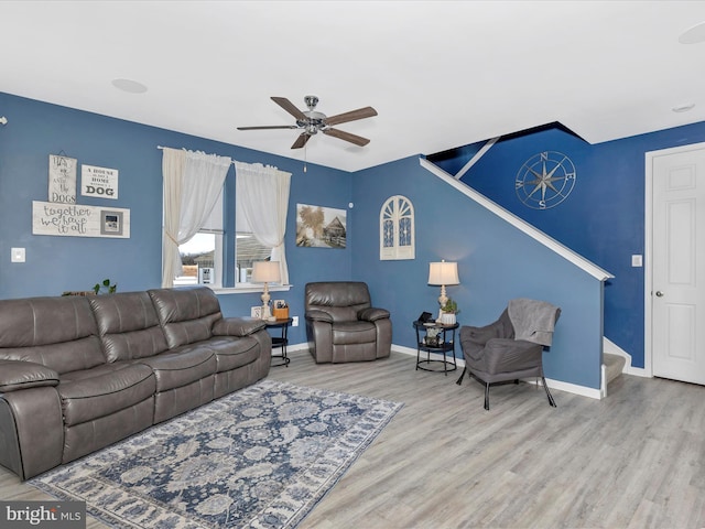 living area featuring a ceiling fan, stairs, baseboards, and wood finished floors