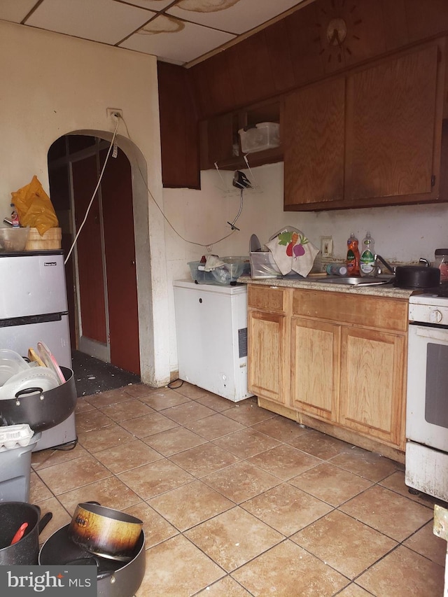 kitchen featuring light tile patterned floors, a drop ceiling, white range oven, refrigerator, and a sink