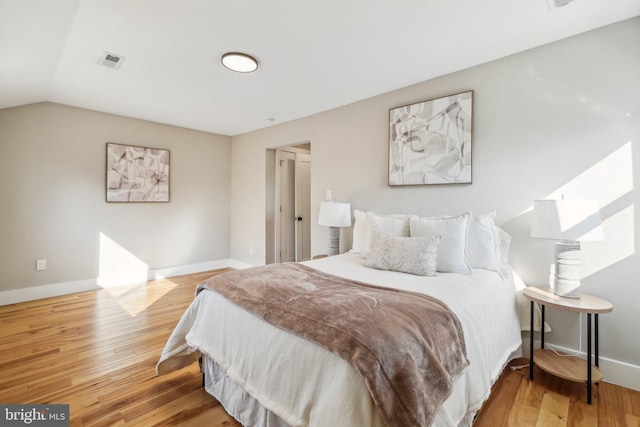 bedroom with lofted ceiling, light wood-style flooring, baseboards, and visible vents