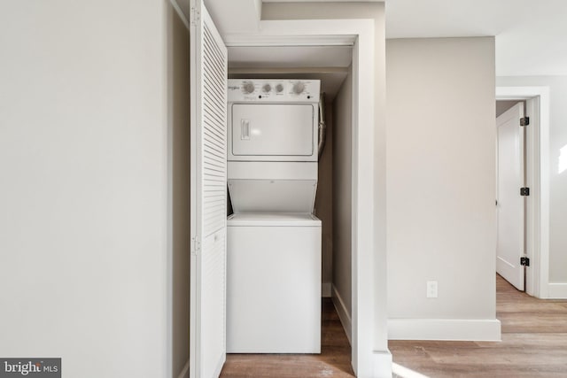 laundry room with stacked washer / drying machine, baseboards, wood finished floors, and laundry area