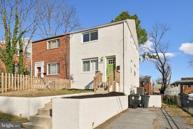 multi unit property featuring cooling unit, brick siding, and a fenced front yard