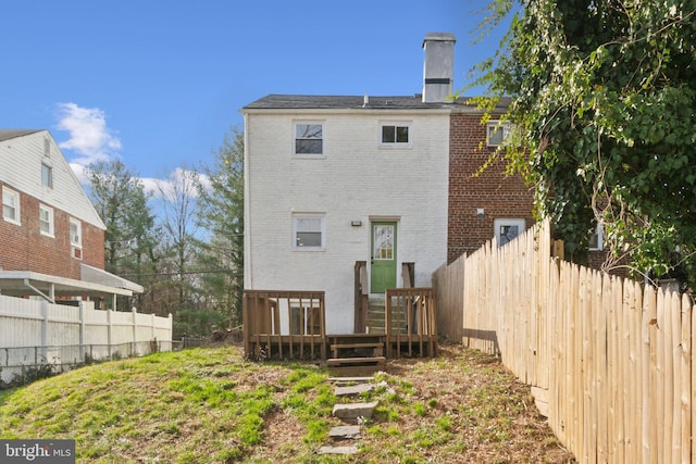 rear view of house with brick siding, a chimney, and fence