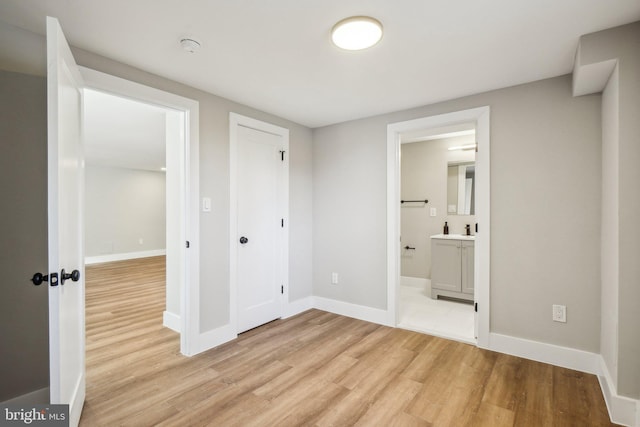 unfurnished bedroom featuring connected bathroom, baseboards, and light wood-style flooring