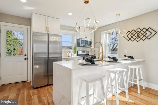 kitchen featuring light wood-style flooring, plenty of natural light, stainless steel appliances, light countertops, and a kitchen bar