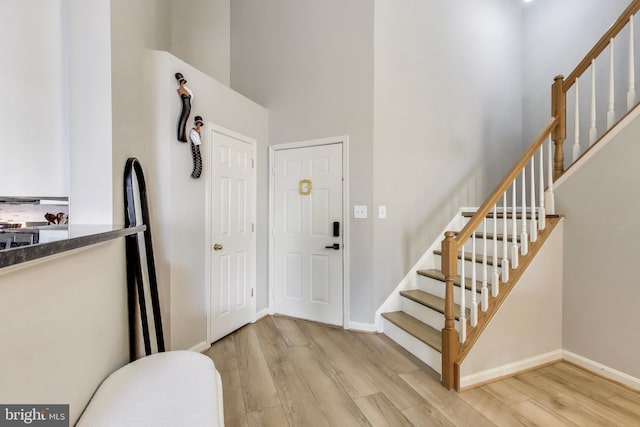 foyer entrance with stairs, light wood finished floors, a high ceiling, and baseboards