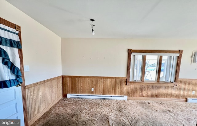 carpeted spare room featuring a baseboard heating unit, wainscoting, and wood walls