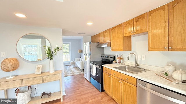 kitchen featuring light wood-style floors, stainless steel appliances, light countertops, under cabinet range hood, and a sink