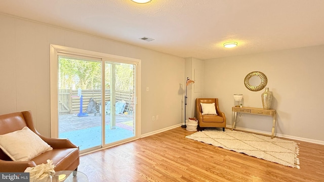 living area featuring a textured ceiling, wood finished floors, visible vents, and baseboards