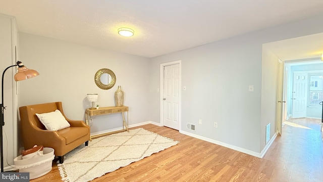 living area with wood finished floors, visible vents, and baseboards