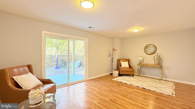 sitting room with baseboards, a textured ceiling, visible vents, and wood finished floors