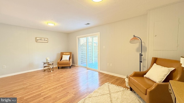 living area featuring baseboards, visible vents, light wood finished floors, and a textured ceiling