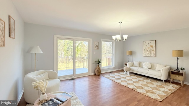 living room featuring baseboards, wood finished floors, visible vents, and an inviting chandelier