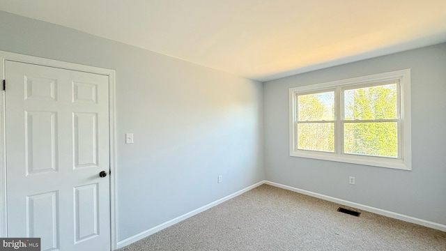 empty room with carpet flooring, visible vents, and baseboards