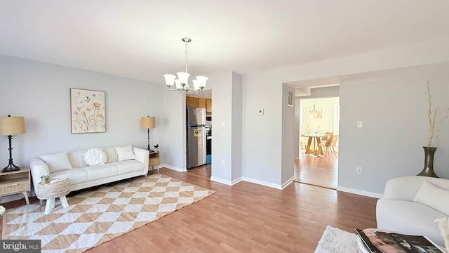 living area featuring light wood-type flooring, visible vents, a notable chandelier, and baseboards