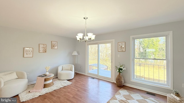 living area with wood finished floors, visible vents, baseboards, and an inviting chandelier